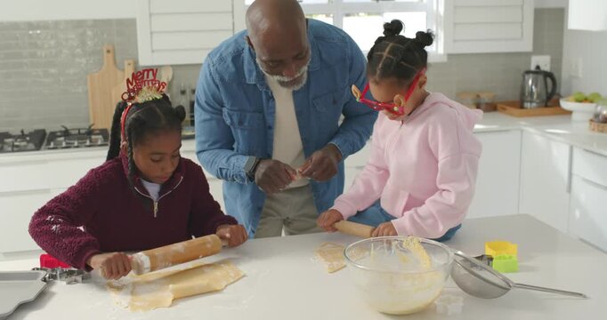 African American family baking on kitchen island christmas urging senior guiding kids rolling dough