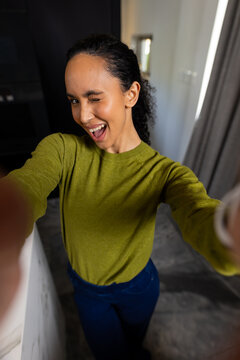 African woman posing and taking selfie in modern kitchen at home with smartphone and wristwatch