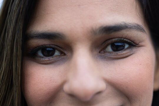 Adult woman facing camera, showing brown eyes, groomed brows and hair strands in tight close-up