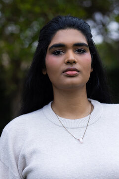 Indian woman posing in garden wearing cream knit sweater and chain necklace with pale pendant