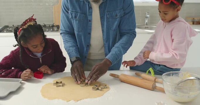 African American family baking at counter senior man guiding girls using star cutters for christmas