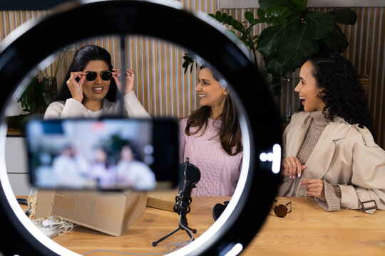 Female collaborators trying on sunglasses while recording in home studio with ring light