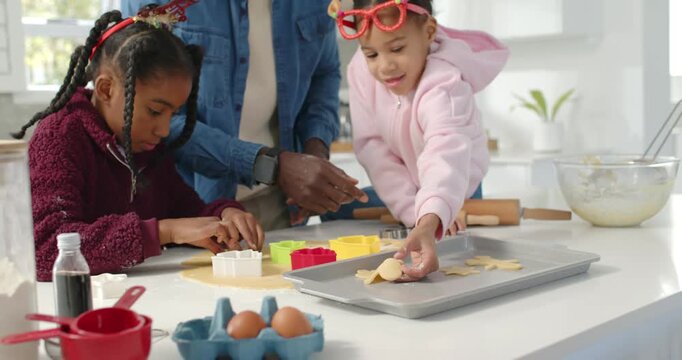 African American man guiding kids making christmas cookies at counter cutting cookies with cutters