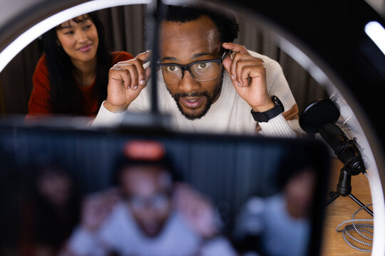 Diverse crew adjusting ring light and mic in studio as African American host with glasses leaning