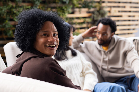 Three friends sitting on patio sofa wearing hoodies and knit sweater beside plants, copy space