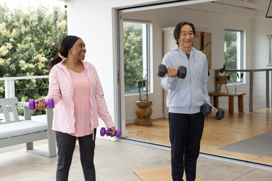 Senior Asian man and Adult woman couple in sportswear holding weights and exercising at home