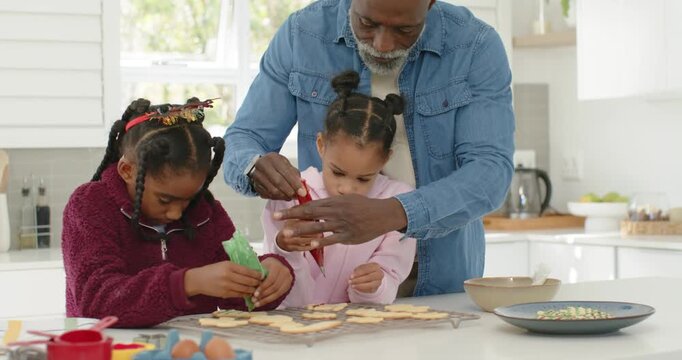 African American family responding to christmas, using piping bags on cookies, dad guiding hands