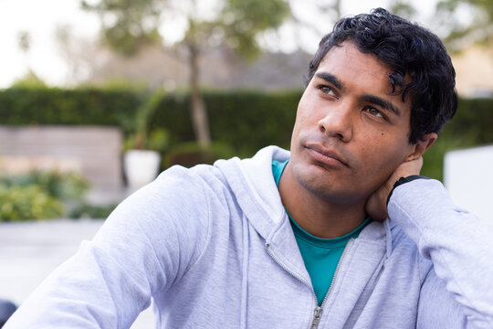 Adult male sitting on patio wearing gray hoodie and teal tee, wristband visible, gazing left