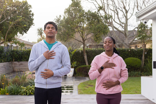 African American couple on deck by path practicing breathing in hoodies with smartwatch visible