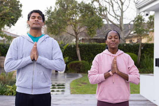 African American couple meditating on backyard deck, pressing palms together while wearing hoodies