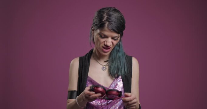 Young woman in sequin top fixing headphones against a pink background