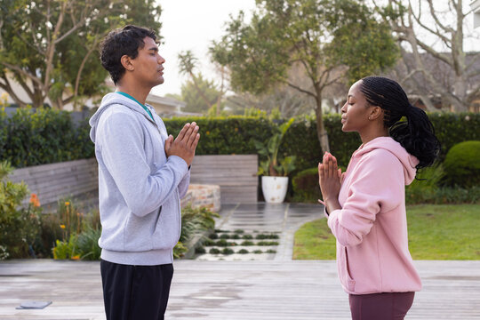 Couple standing facing each other on wooden deck in backyard, pressing palms together