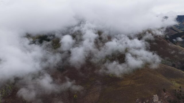 Aerial of thick low clouds and mist rolling over the mountain slopes and rocky terrain in Crested Butte Colorado during the autumn fall colors season