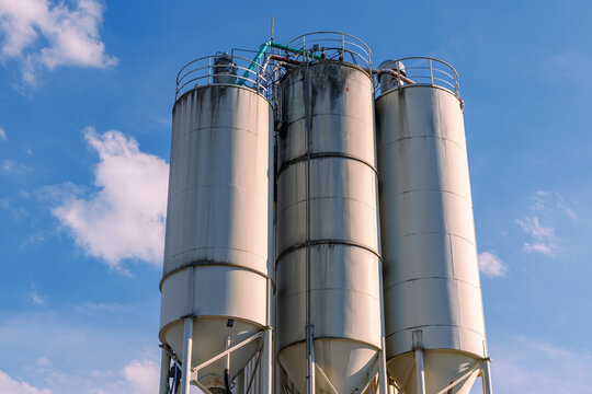 Low angle view of three industrial concrete storage silos against blue sky with light clouds, construction materials and industrial infrastructure concept
