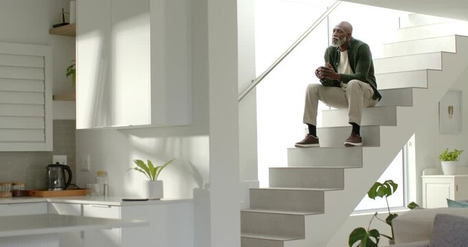 Senior man sitting on floating staircase, sunlight causing christmas smile, reaching mug