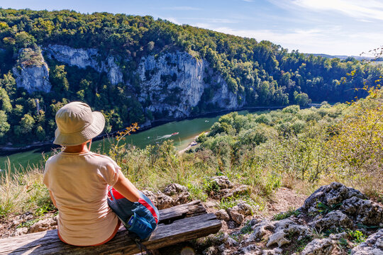 Hiker sitting on wooden bench at scenic viewpoint overlooking Danube river gorge and steep limestone cliffs in Bavaria Germany, active retirement and outdoor travel concept