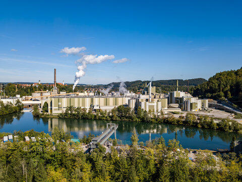 Aerial view of a large modern industrial plant and paper factory next to a river surrounded by green forests, industrial landscape and environmental concepts