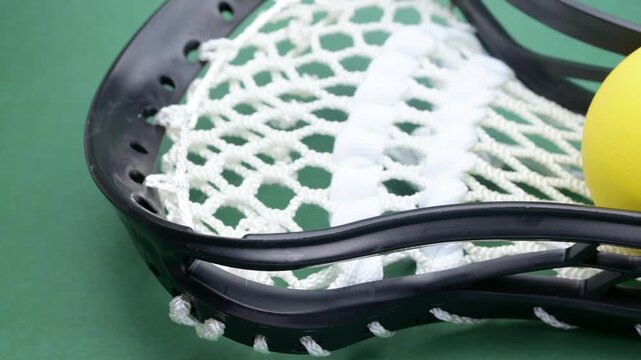 pan view yellow lacrosse ball rests on the head of a black lacrosse stick with white netting