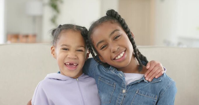 African American sisters, children, older placing arm around younger on sofa, smiling for christmas