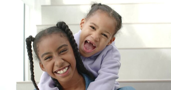 African American child sisters laughing on stairs at christmas, younger sister hugging, nuzzling