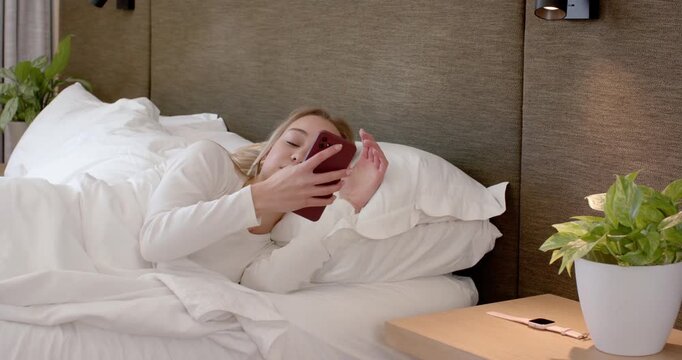 Female waking, reaching for red phone on nightstand picking up and checking it then stretching