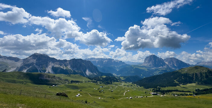  idyllic rolling hills landscape with blooming meadows and alpine mountain peaks in the background on a beautiful sunny day with blue sky and clouds, Alpe di Cisles, Seceda Ridgeline, Dolomiti 