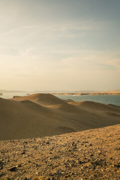 View of the arid desert landscape and sand dunes of Paracas National Reserve meeting the Pacific Ocean coastline in Paracas, Ica, Peru.