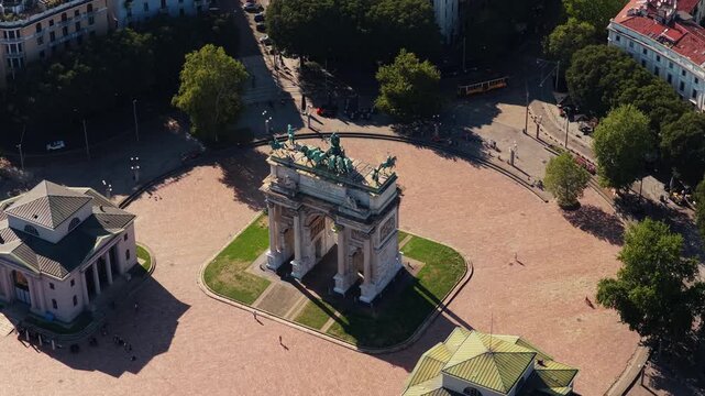 Close aerial view of Arco della Pace topped by bronze chariot statues in Milan, Italy, orange tram and few pedestrians around Piazza Sempione on a sunny day