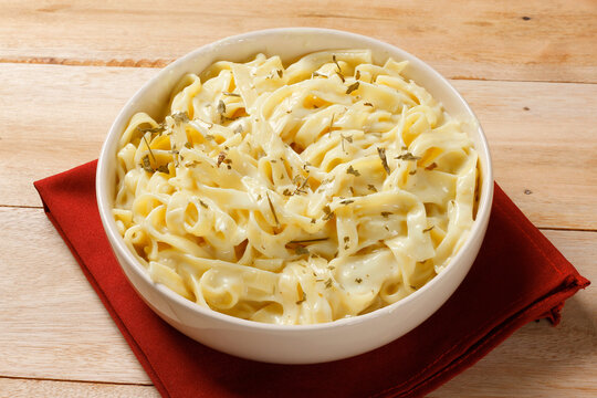 Fettuccine pasta in a white cheese sauce, served in a white bowl and finished with fresh basil on a wooden table.