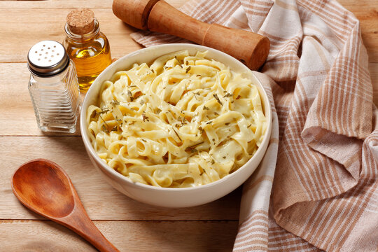 Creamy Fettuccine Alfredo with cheese sauce served in a white bowl with herbs on a wooden table.