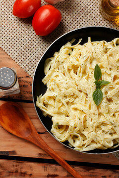 Fettuccine Alfredo in a white cheese sauce, served in a black skillet with fresh basil in a rustic setting.