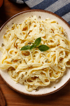 Fettuccine Alfredo with cheese sauce on a rustic plate, accompanied by fresh basil, on a rustic table.