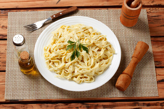 Italian Fettuccine Alfredo with a creamy white cheese texture, served on a white ceramic plate with basil on a wooden surface.