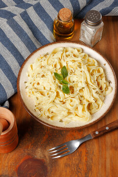 Fettuccine Alfredo pasta coated in a creamy white cheese sauce, served on a rustic plate with basil leaves, set on a rustic wooden surface.