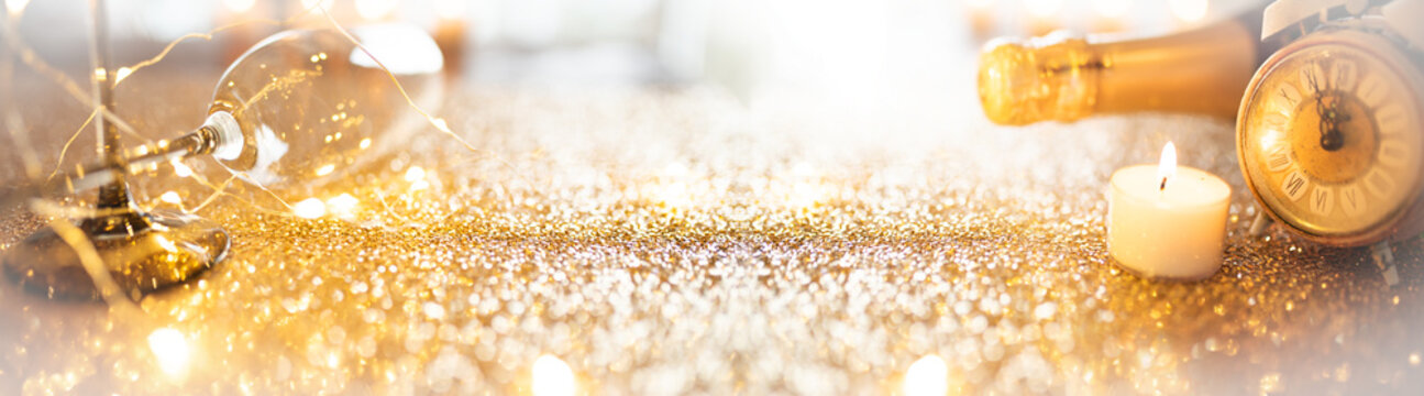 Gold glittering texture for a party, featuring champagne and a clock. Long horizontal new year's eve background at twelve o'clock. Space for text.