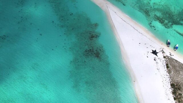 Aerial view of Los Roques archipelago featuring white sand beach, turquoise water, small boats, and a sunshade in Los Roques, Dependencias Federale, Venezuela.