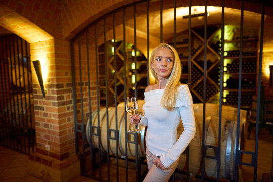 Beautiful Blonde Woman Enjoying White Wine Tasting in a Winery Cellar