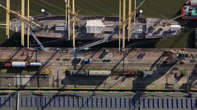 Top down view rising above the full length of the historic four-masted barque Peking and a red workboat in the port of Hamburg, Germany, solar roofs and long shadows