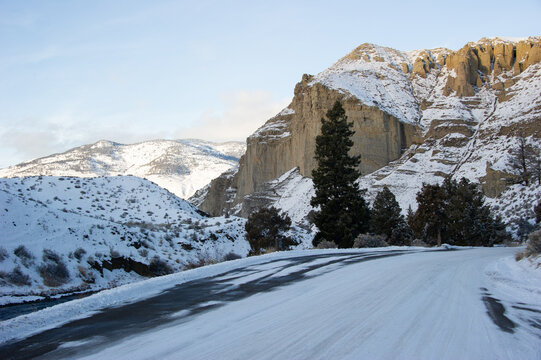 View of a snow-covered road winding through the rugged, snow-capped mountains and evergreen trees of Yellowstone National Park, United States.