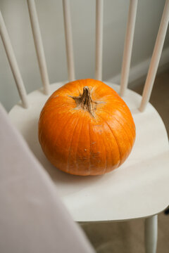Orange pumpkin on a white chair in a minimalist home interior, warm autumn seasonal decoration with natural light, fall Halloween and Thanksgiving concept with copy space