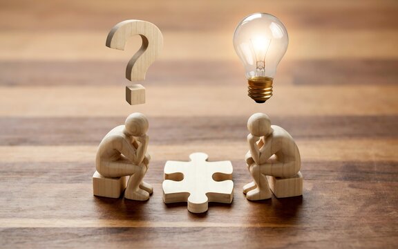 Wooden figurines sitting with puzzle piece question mark and glowing lightbulb symbol representing problem solving and creative thinking in business development.