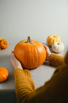 Woman holding an orange pumpkin at home during autumn, orange and white pumpkins in a rustic wicker basket, cozy seasonal lifestyle scene for Halloween, Thanksgiving and fall concepts