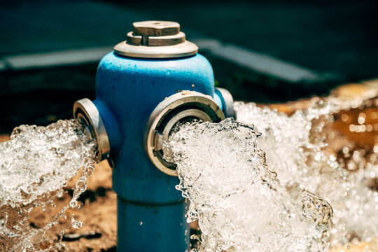 Blue fire hydrant releasing a powerful stream of water during system flushing. Urban infrastructure, water distribution and maintenance operation theme.