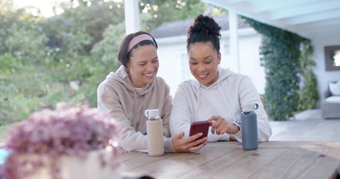 Two female friends leaning in, right woman showing red phone, scrolling messages, reacting on porch