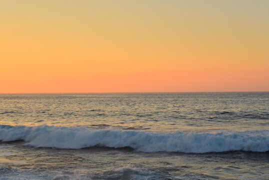 A moment of a peaceful sunset by the sea, with gentle waves and a sky tinged with golden hues.