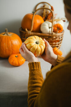 Woman holding a small pumpkin at home during autumn, orange and white pumpkins in a rustic wicker basket, cozy seasonal lifestyle scene for Halloween, Thanksgiving and fall concepts