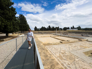 Obraz premium woman exploring ancient ruins with mosaic floors and stone columns, wide angle shot from a slight elevation, blue sky and white clouds in the background, modern and serene atmosphere, ideal.
