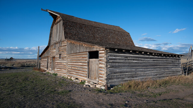 View of the historic wooden barn in Jackson Hole, featuring weathered timber walls and a shingled roof under a clear blue sky in Teton County, Wyoming, United States.