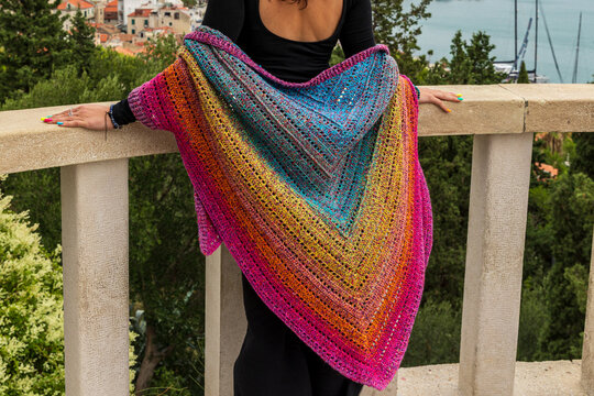 Vibrant handmade crochet triangle shawl displayed on young woman outdoors with scenic city background