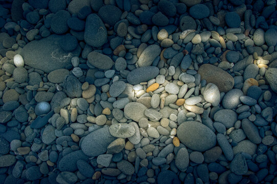 View of smooth rounded beach pebbles and stones illuminated by dappled sunlight at Olympic National Park in Port Angeles, Washington, United States.